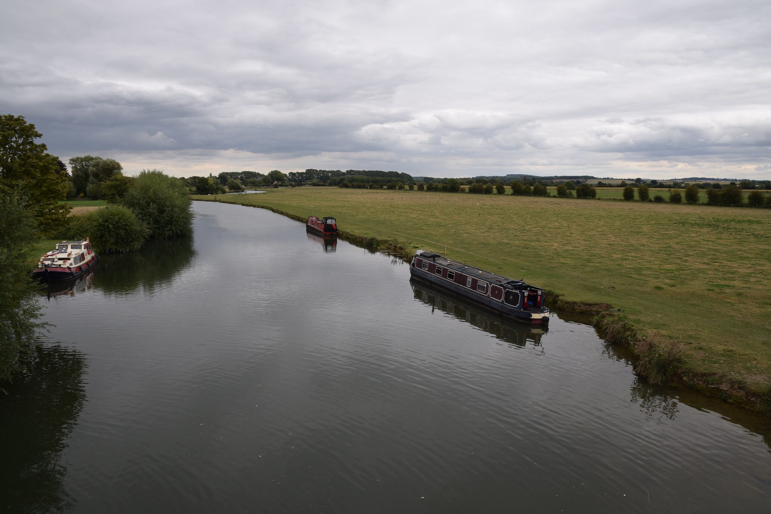 The River Thames winding between flat water meadows below Lechlade, with narrowboats moored along the bank