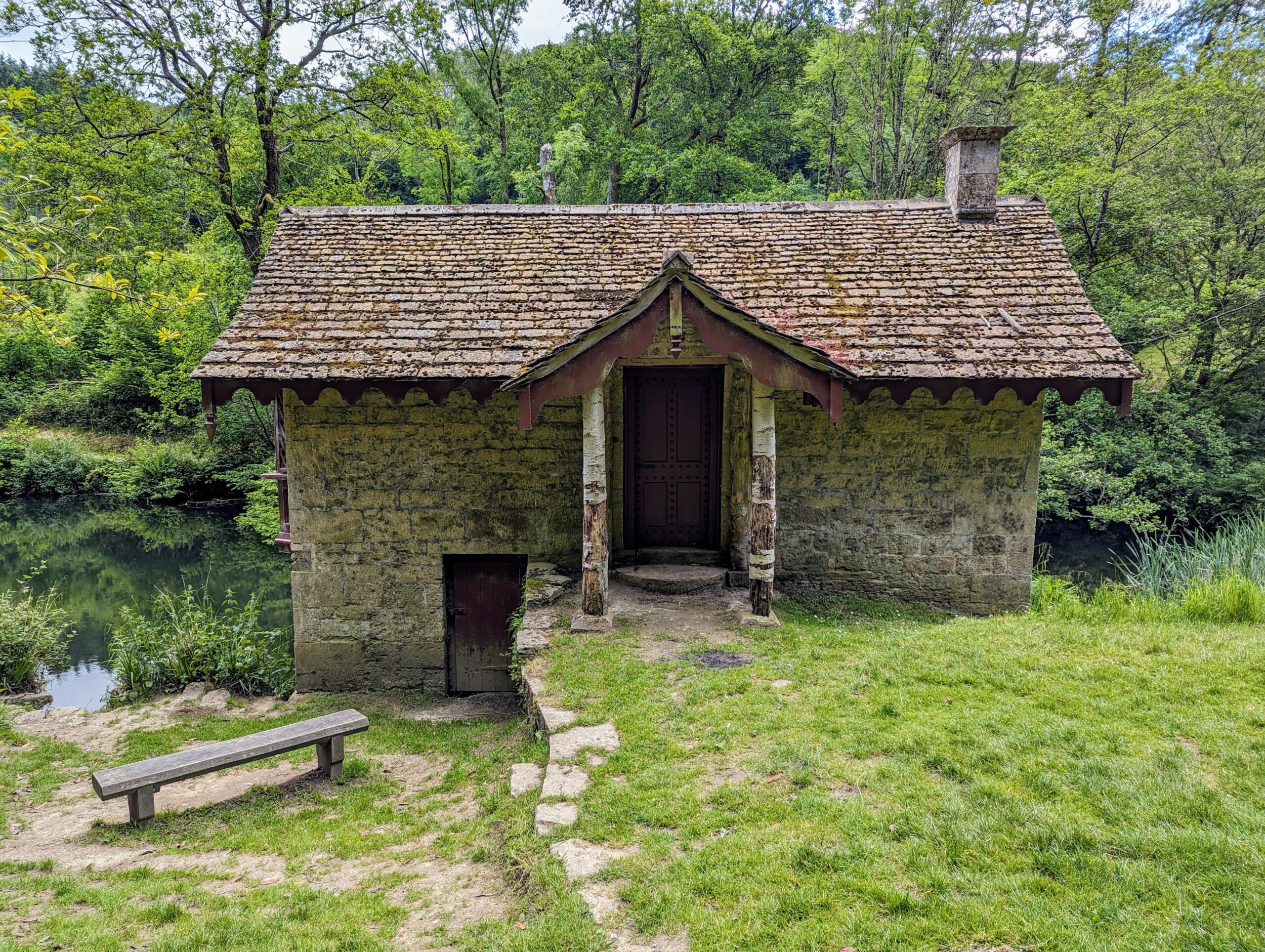 The small stone boathouse with a tiled roof and wooden porch beside one of the lakes in Woodchester Park